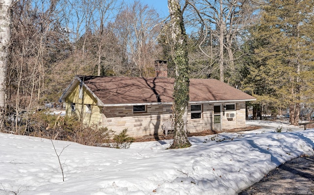 view of snowy exterior featuring stone siding, a chimney, and cooling unit