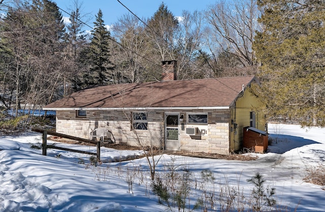 view of front of home with stone siding, a chimney, cooling unit, and roof with shingles