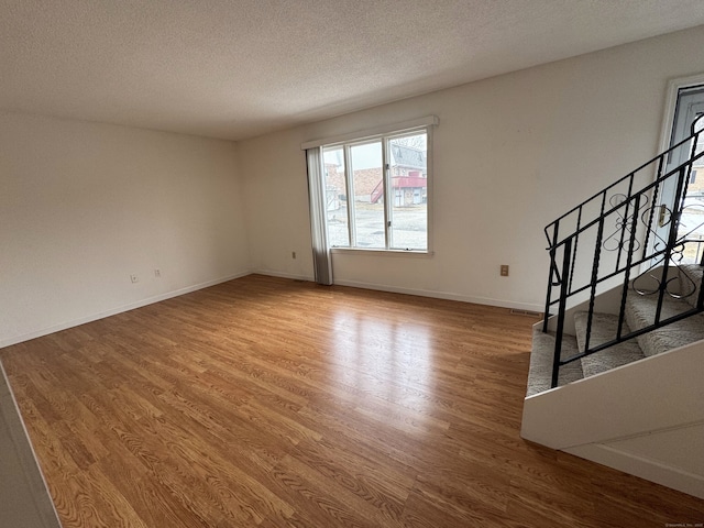 unfurnished living room featuring baseboards, a textured ceiling, stairway, and wood finished floors