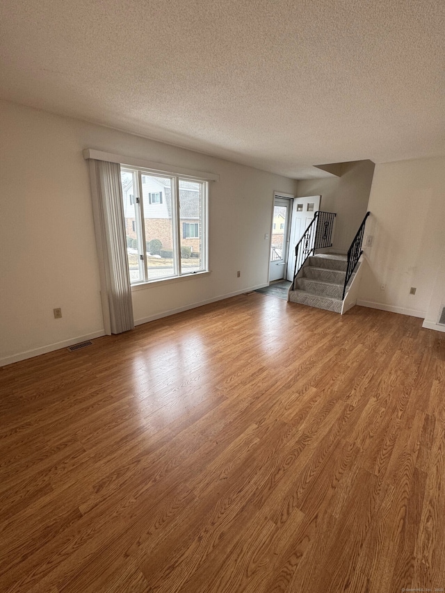 unfurnished living room featuring baseboards, visible vents, stairway, wood finished floors, and a textured ceiling