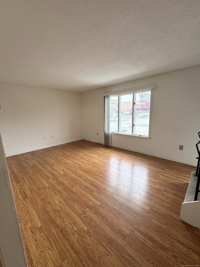 unfurnished room with visible vents, baseboards, a textured ceiling, and light wood finished floors