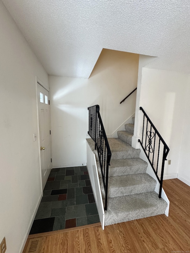 staircase with a textured ceiling, baseboards, and wood finished floors