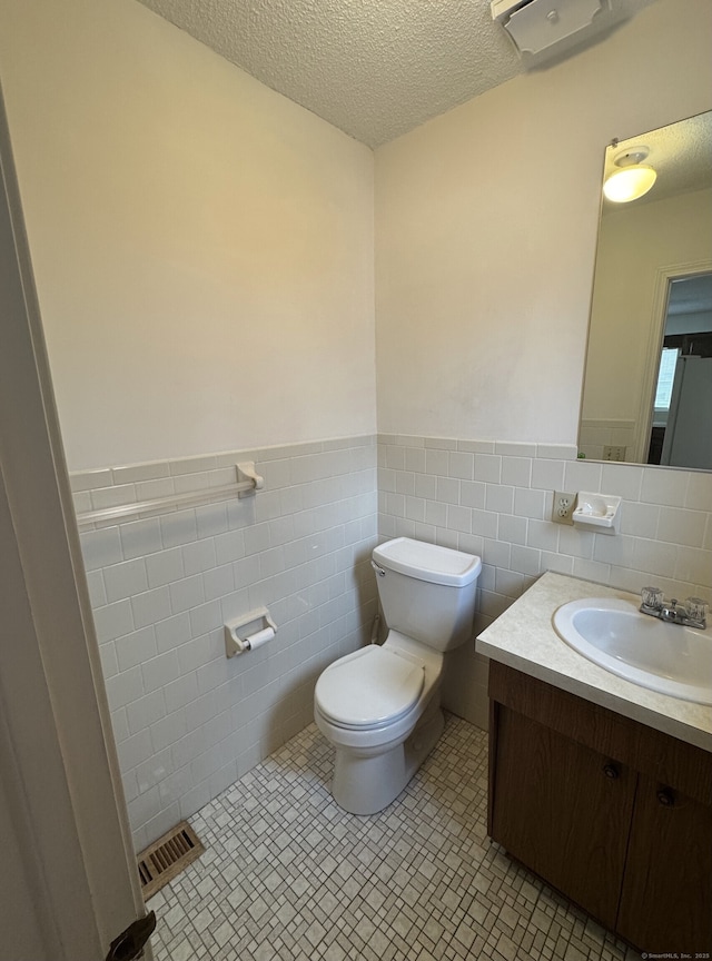 bathroom with a textured ceiling, toilet, vanity, and visible vents