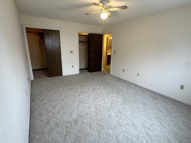 unfurnished bedroom featuring a textured ceiling, carpet floors, two closets, and baseboards