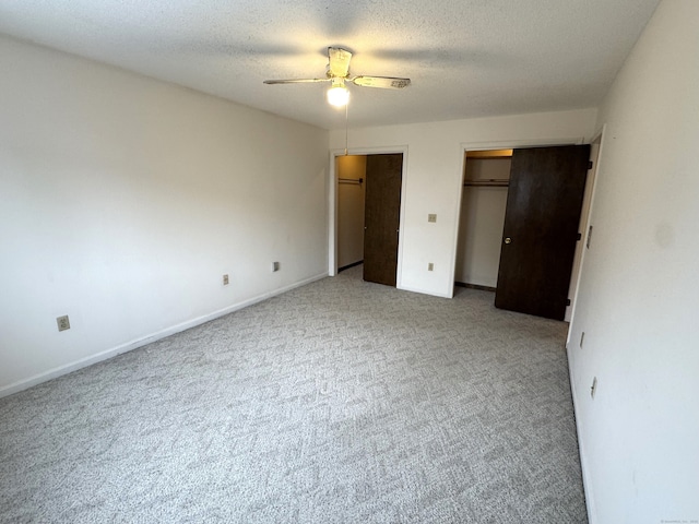 unfurnished bedroom featuring a textured ceiling, carpet flooring, two closets, and baseboards