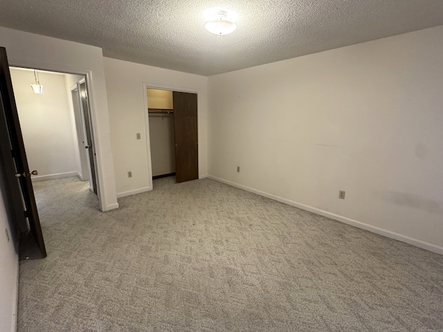 unfurnished bedroom featuring light carpet, a closet, a textured ceiling, and baseboards