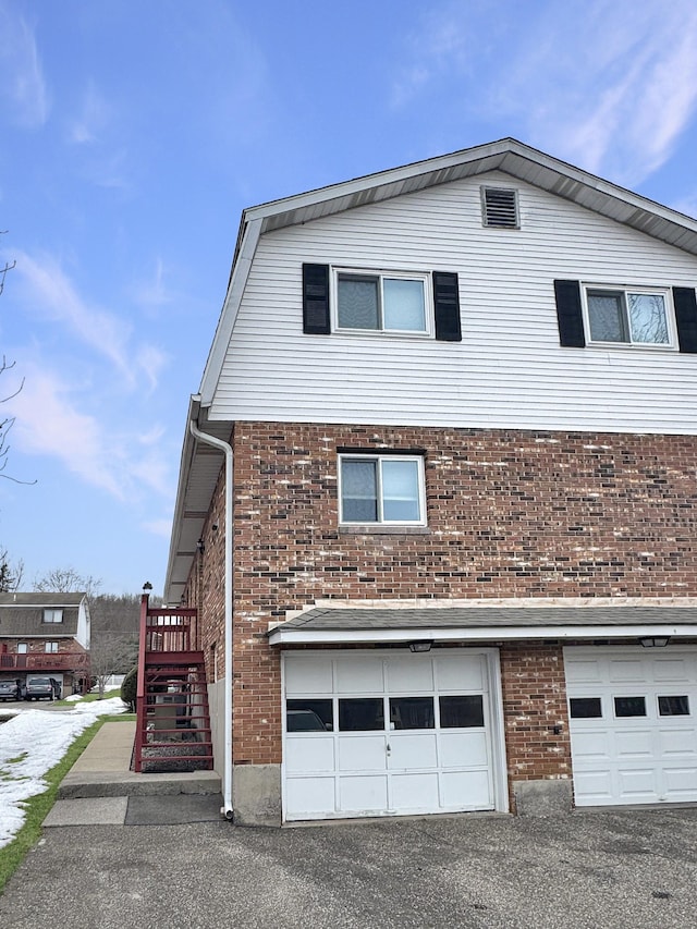 view of side of home with aphalt driveway, brick siding, a gambrel roof, an attached garage, and stairs