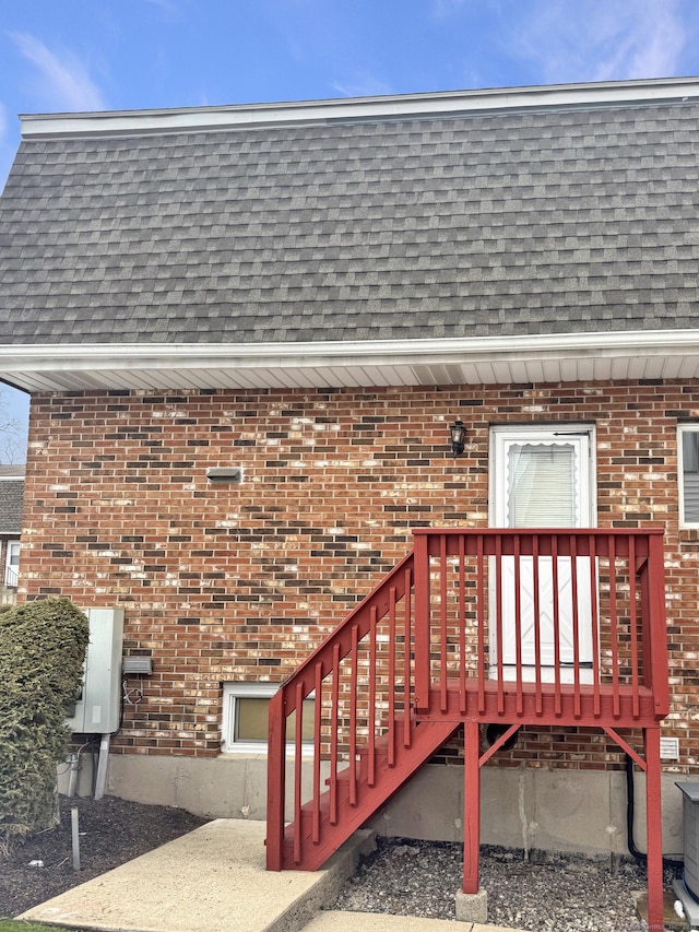 property entrance with roof with shingles, brick siding, a wooden deck, and mansard roof