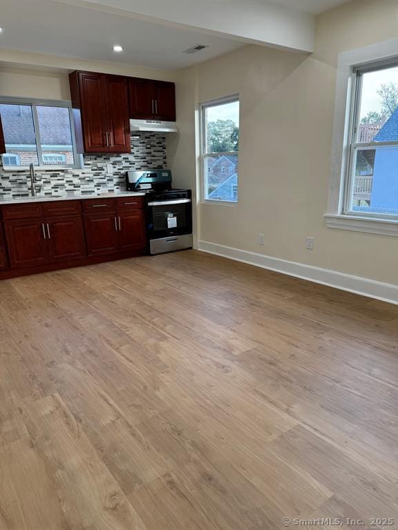 kitchen with a sink, light wood finished floors, electric stove, light countertops, and tasteful backsplash