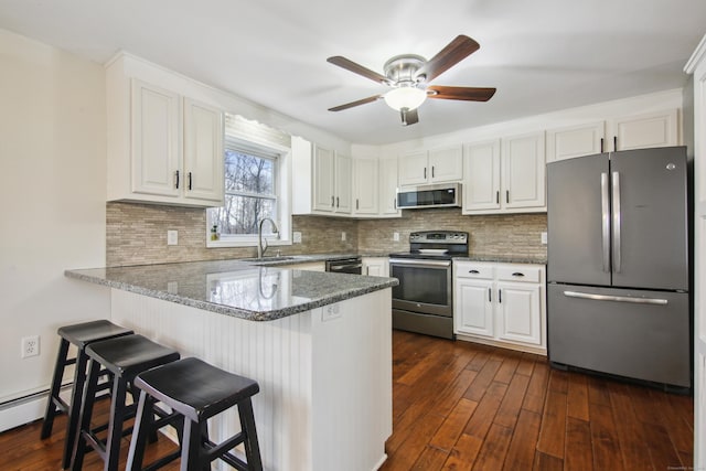 kitchen with stainless steel appliances, dark wood-type flooring, a peninsula, a sink, and white cabinetry