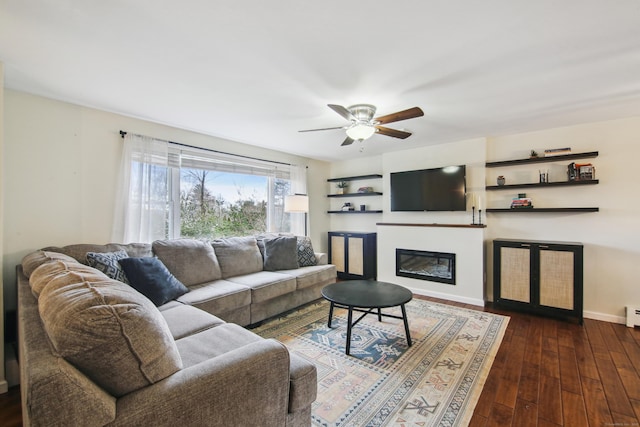 living room with a ceiling fan, baseboards, dark wood-style flooring, and a glass covered fireplace