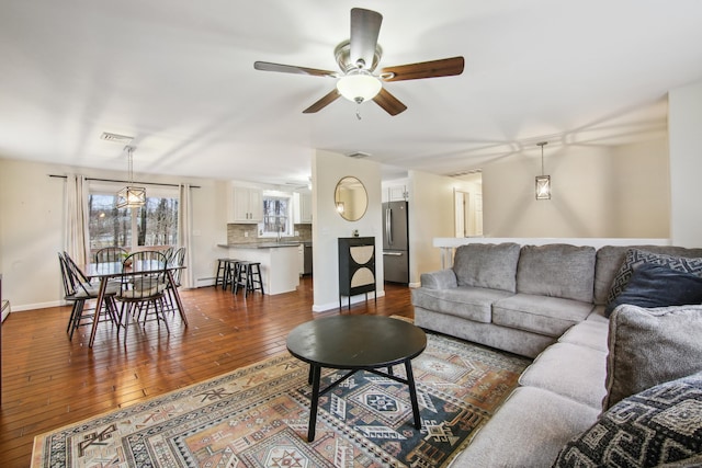 living room featuring dark wood-style floors, visible vents, a ceiling fan, and baseboards