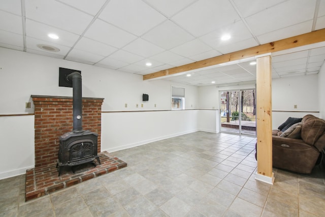 basement with a paneled ceiling, recessed lighting, a wood stove, and baseboards