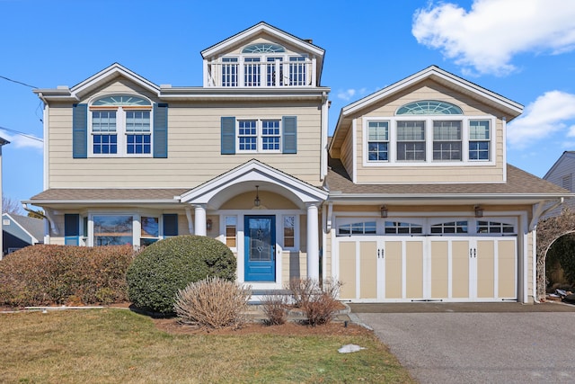 view of front facade featuring driveway, a garage, a balcony, roof with shingles, and a front lawn