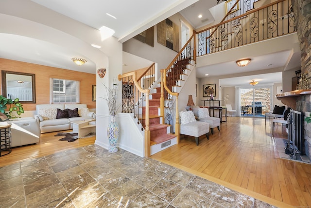 living area with a large fireplace, hardwood / wood-style floors, stairs, and a towering ceiling