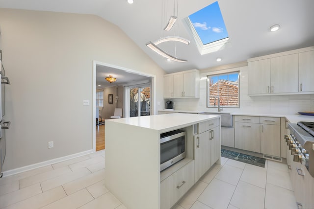 kitchen featuring light tile patterned floors, vaulted ceiling with skylight, stainless steel microwave, light countertops, and a sink