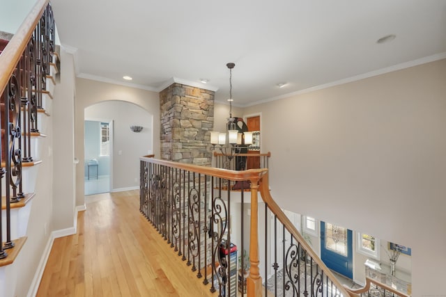 corridor with arched walkways, crown molding, an upstairs landing, wood finished floors, and baseboards