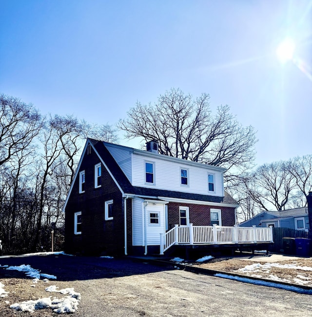 view of front of property with brick siding, a chimney, and a wooden deck