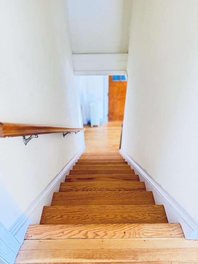 staircase with baseboards, radiator heating unit, and wood finished floors