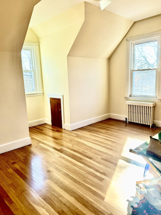 bonus room with lofted ceiling, light wood-style floors, baseboards, and radiator