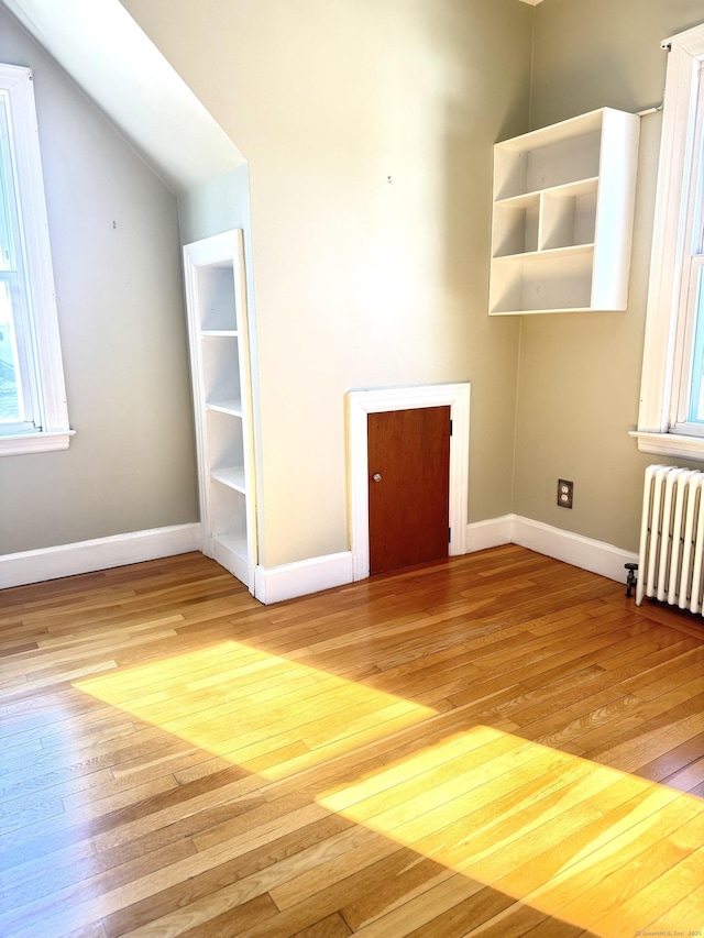 unfurnished living room with light wood finished floors, radiator heating unit, baseboards, and vaulted ceiling