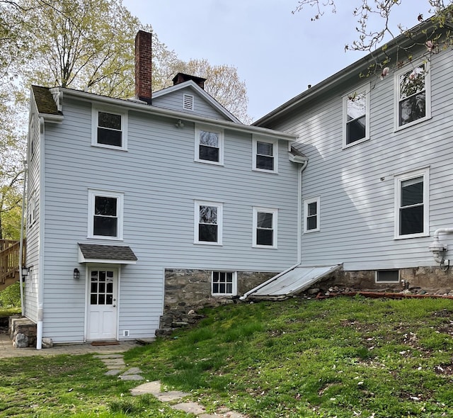 rear view of property featuring a chimney and a lawn