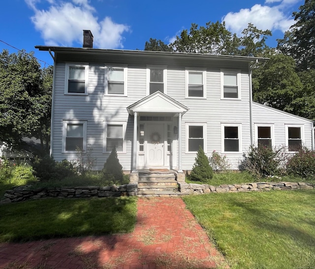 colonial home featuring a chimney and a front yard