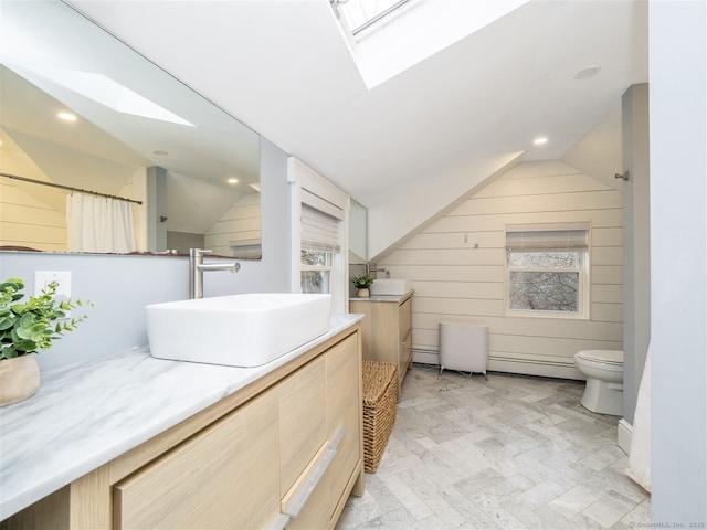 full bath featuring wooden walls, toilet, lofted ceiling with skylight, baseboard heating, and vanity