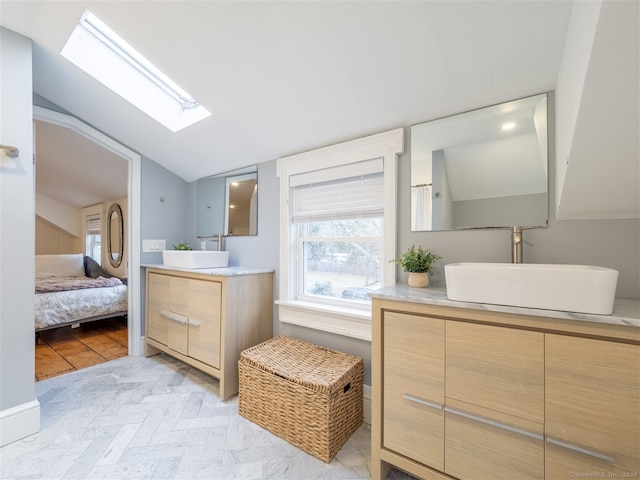 ensuite bathroom featuring ensuite bath, vaulted ceiling with skylight, two vanities, and a sink