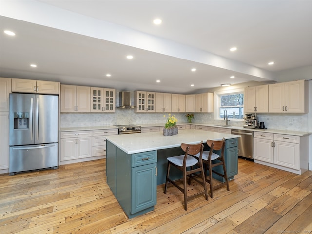 kitchen with light wood finished floors, wall chimney exhaust hood, appliances with stainless steel finishes, and a sink