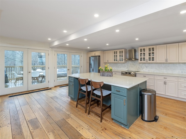 kitchen with french doors, stainless steel appliances, light countertops, a kitchen island, and wall chimney range hood