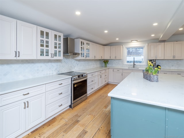 kitchen with electric range, a sink, light wood-type flooring, wall chimney exhaust hood, and tasteful backsplash