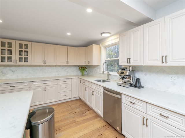 kitchen featuring a sink, light countertops, light wood-type flooring, decorative backsplash, and dishwasher