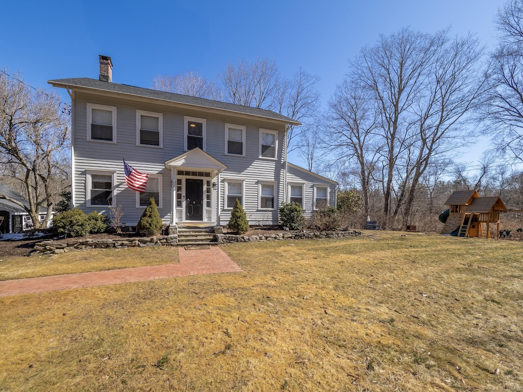 colonial inspired home featuring a chimney, a front lawn, and a playground
