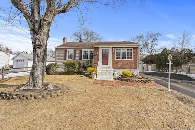 view of front of property with aphalt driveway, brick siding, a chimney, entry steps, and a front yard