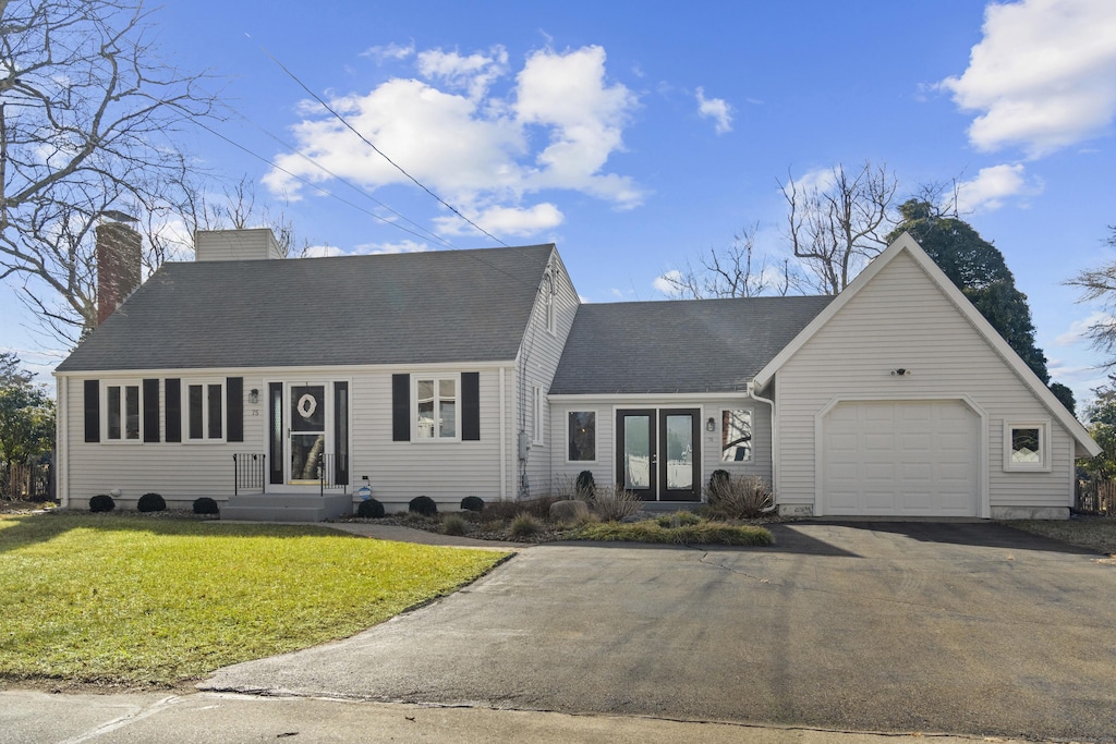 cape cod house with a front yard, an attached garage, a shingled roof, a chimney, and aphalt driveway