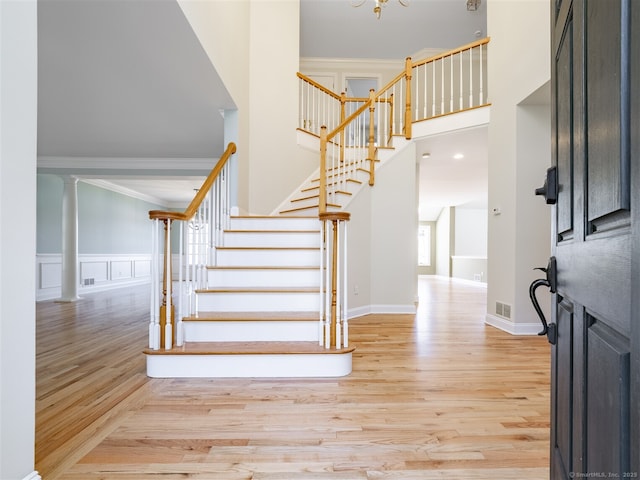 stairway with visible vents, wood finished floors, a high ceiling, crown molding, and a decorative wall