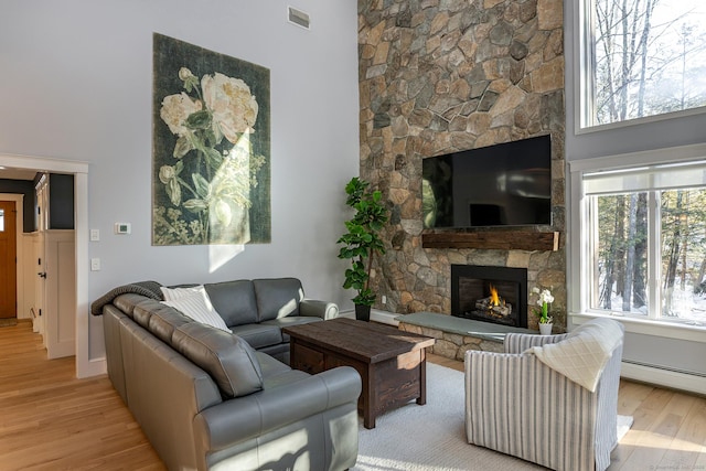 living area with a baseboard radiator, a fireplace, wood finished floors, visible vents, and a towering ceiling