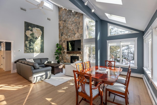 dining area featuring a fireplace, visible vents, baseboard heating, light wood-type flooring, and lofted ceiling with skylight