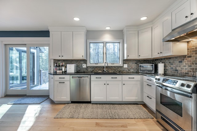 kitchen featuring stainless steel appliances, dark countertops, a sink, and under cabinet range hood