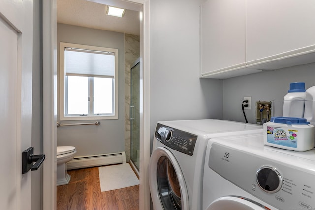 laundry room with a baseboard heating unit, cabinet space, washing machine and clothes dryer, and wood finished floors