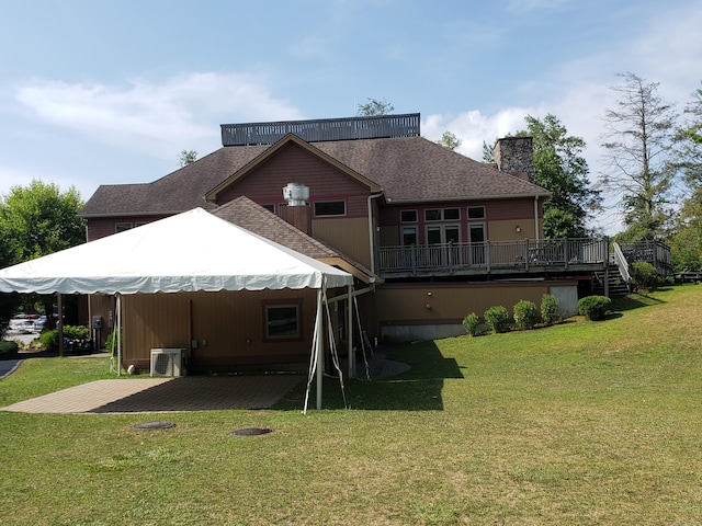 back of house with a deck, a shingled roof, a yard, a chimney, and a patio area