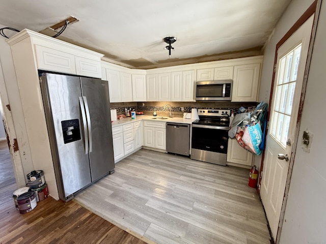 kitchen featuring light wood-style flooring, stainless steel appliances, a sink, white cabinetry, and light countertops