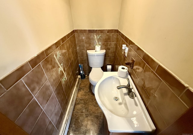 bathroom featuring tile walls, wainscoting, toilet, a baseboard radiator, and a sink