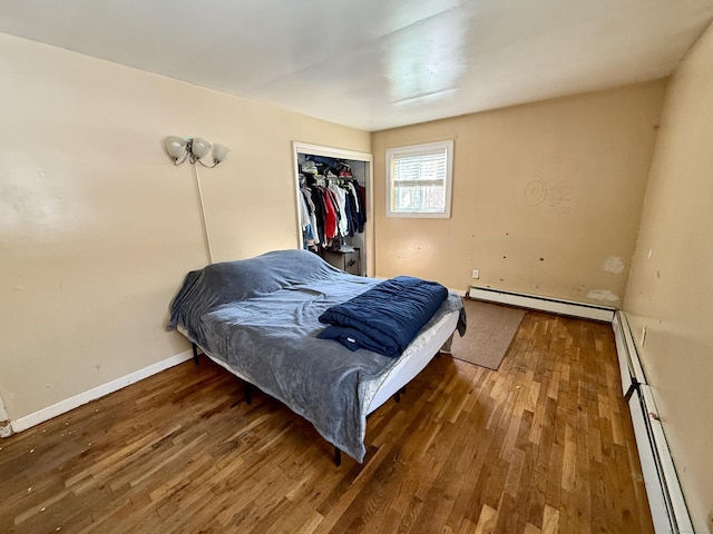 bedroom featuring dark wood-type flooring, baseboard heating, a closet, and baseboards