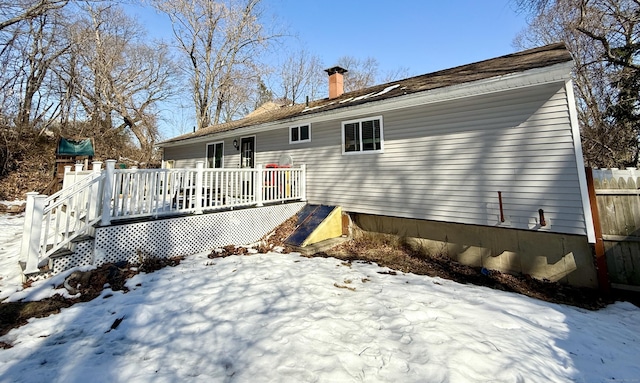 snow covered rear of property with a chimney, fence, and a wooden deck