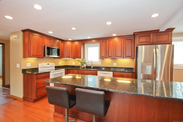 kitchen featuring light wood finished floors, dark stone counters, recessed lighting, a sink, and stainless steel appliances