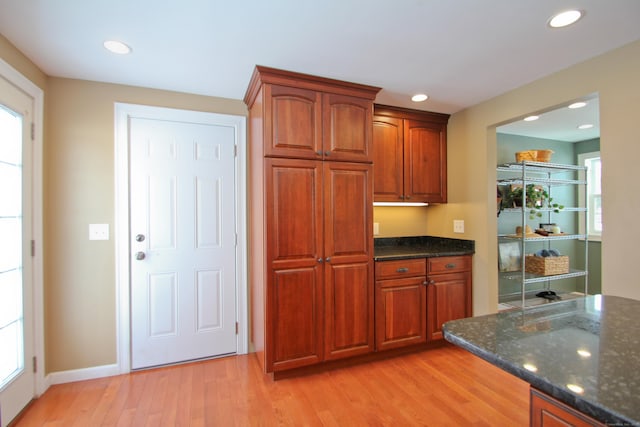 kitchen with dark stone countertops, light wood-style flooring, brown cabinetry, and recessed lighting