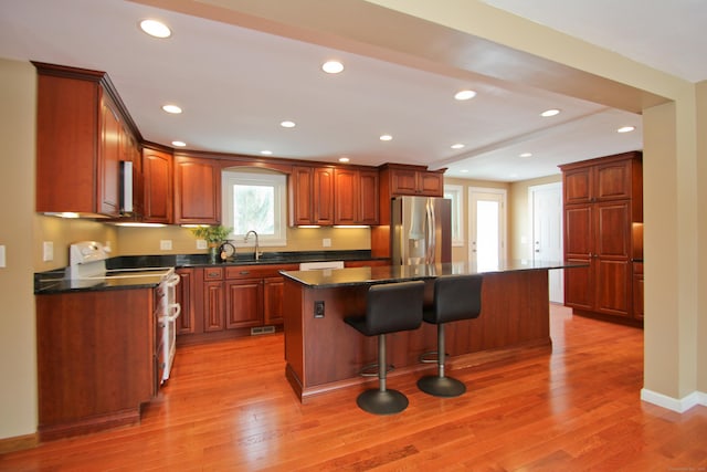 kitchen with a sink, range with electric stovetop, dark countertops, a kitchen island, and stainless steel fridge