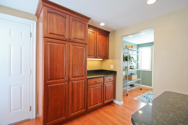 kitchen featuring light wood-type flooring, brown cabinets, recessed lighting, dark stone counters, and baseboards